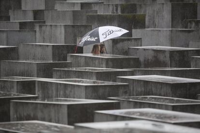 Dos mujeres pasean cubiertas con un paraguas para protegerse de la lluvia entre los bloques de cemento del Monumento al Holocausto en Berlín (Alemania).