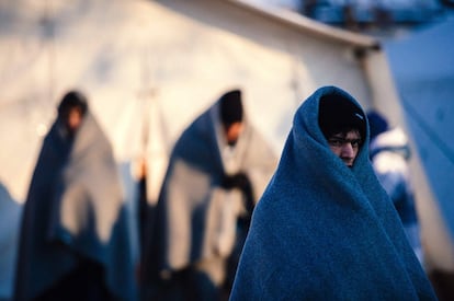 Un grupo de inmigrantes cubiertos con mantas para paliar el frío esperan para ser registrados en el campo de Presevo, Serbia.