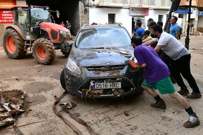 Voluntarios y residentes retiran un vehículo con ayuda de un tractor en Sedaví (Valencia), este domingo. 