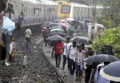 La gente camina en una vía férrea después de apearse de un tren local, que no pudo avanzar debido a las inundaciones en las áreas de Mumbai (India).