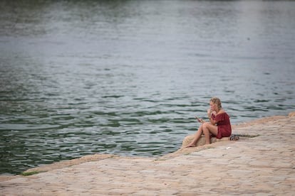 Una joven, sentada  junto al río en Sevilla.
