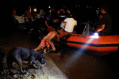 Un hombre sujeta a un perro y empuja una barca hinchable en Mati, durante los desalojos por los incendios.