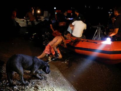 Un hombre sujeta a un perro y empuja una barca hinchable en Mati, durante los desalojos por los incendios.