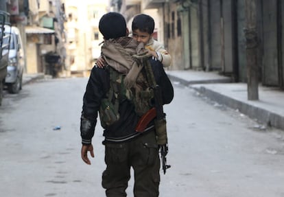 Un combatiente kurdo de las Unidades de Protección Popular (YPG) lleva a su hijo a través de una calle de del barrio Sheikh Maqsoud de Alepo.