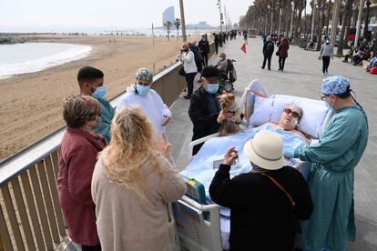 Amigos, vecinos y personal médico rodean a la paciente de covid Marta Pascual, de 72 años, mientras toma aire fresco en la playa de la Barceloneta, frente al Hospital del Mar en Barcelona.