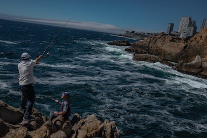 Dos pescadores sobre las rocas oceánicas de Concón, con vista a las edificaciones del borde costero.