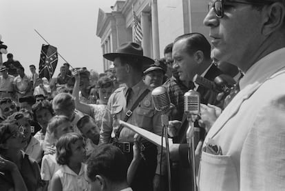 Un grupo de personas, una de ellas con la bandera confederada, en 1959 en la puerta del Congreso estatal de Arkansas, rodean a unos portavoces mientras protestan la admisión en una escuela de nueve niñas negras