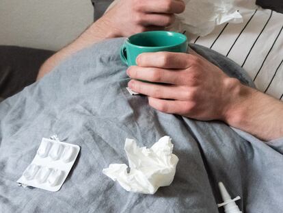 Un hombre descansa en la cama con medicamentos para el catarro y pañuelos.