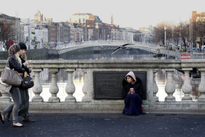 Dos mujeres caminan por un puente en Dublín ante la mirada de una mendiga.