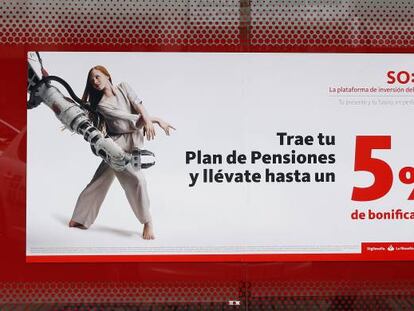 Una mujer camina delante de un cartel anunciando planes de pensiones, en una oficina de Banco Santander, en Madrid.