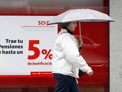 Una mujer camina delante de un cartel anunciando planes de pensiones, en una oficina de Banco Santander, en Madrid.