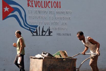Un hombre empuja una carretilla junto a un cartel alusivo a la revolución en La Habana.
