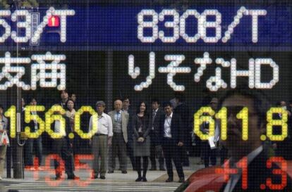 Varios peatones se reflejan en una pantalla con informaci&oacute;n burs&aacute;til en Tokio.