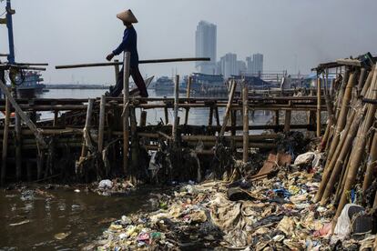Un hombre camina por encima de la basura en un pueblo de pescadores en Jakarta (Indonesia).