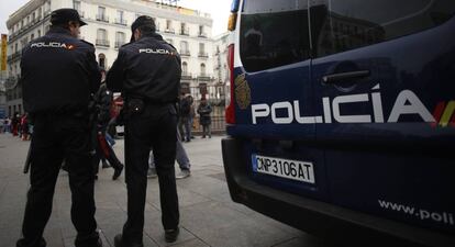 Dos agentes de la Policía Nacional, de pie, junto a un furgón. 