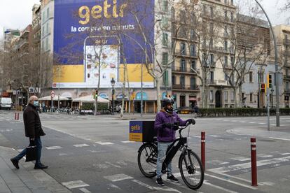 Un repartidor del supermercado en línea de entregas rápidas Getir ante una pancarta de la misma empresa, en Barcelona.