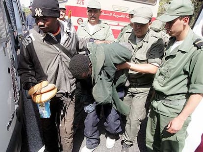 Agentes de Marruecos conducen a dos subsaharianos apresados en el entorno de Ceuta hasta un furgón policial.