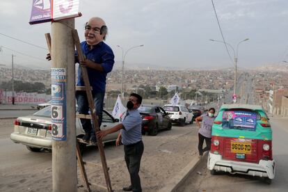 Un hombre con una máscara que representa al candidato presidencial Hernando de Soto del partido Avanza País coloca una pancarta antes de un evento en el barrio de Villa El Salvador en Lima, Perú, el 5 de abril.