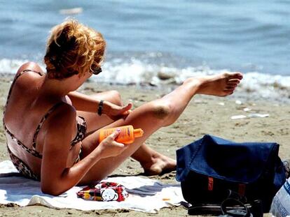 Una mujer se aplica crema protectora en una playa.