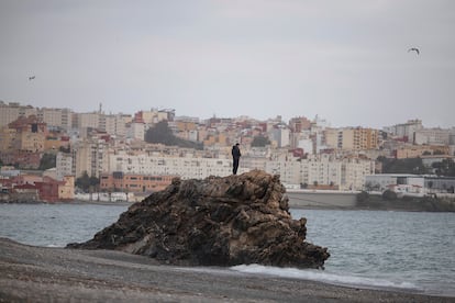 Un joven subido a una roca en la playa del Tarajal, el 22 de marzo;  al fondo, la ciudad de Ceuta.