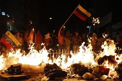 Manifestantes de la oposición sostienen una bandera venezolana ante una barricada ardiendo.