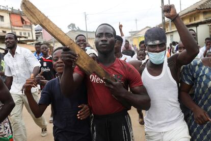 Un manifestante en Costa de Marfil sostiene un arma de madera, junto a otro con mascarilla, durante la marcha un día después de los enfrentamientos con la policía. El presidente del país, Alassane Ouattara, se ha postulado para un tercer mandato en las próximas elecciones presidenciales.