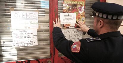Un polic&iacute;a municipal coloca un cartel en una tienda clausurada por venta de alcohol a menores en Madrid 
 