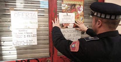 Policial municipal coloca um cartaz numa loja fechada por vender bebida alcoólica a menores em Madri.