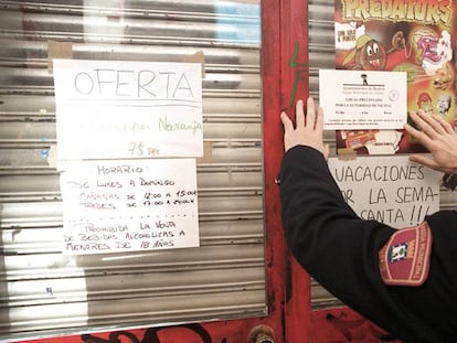 Policial municipal coloca um cartaz numa loja fechada por vender bebida alcoólica a menores em Madri.