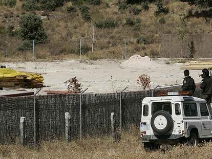 Unos agentes forestales vigilan el interior de una finca desde la valla exterior.