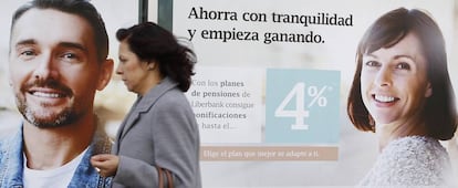 Una mujer pasa delante de una sucursal bancaria donde se anuncian planes de pensiones.