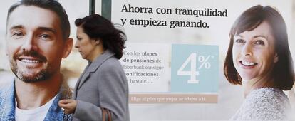 Una mujer pasa delante de una sucursal bancaria donde se anuncian planes de pensiones.