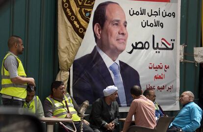 Varios egipcios conversan frente a un cartel de Al Sisi en el que se lee