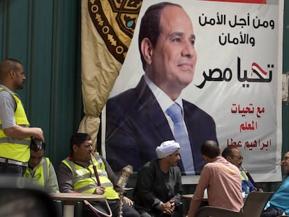 Varios egipcios conversan frente a un cartel de Al Sisi en el que se lee