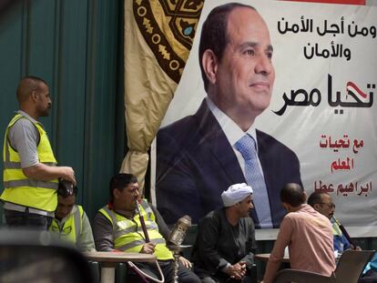 Varios egipcios conversan frente a un cartel de Al Sisi en el que se lee