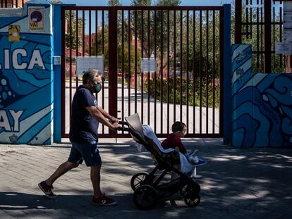 Un hombre pasa con un bebé esta mañana por la puerta del colegio Republica del Uruguay, en el distrito de Latina.