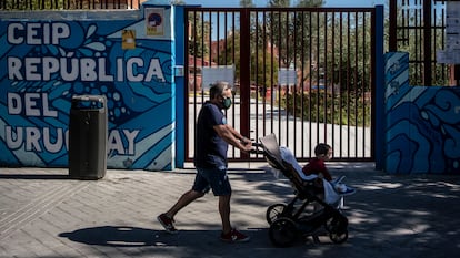 Un hombre pasa con un bebé esta mañana por la puerta del colegio Republica del Uruguay, en el distrito de Latina.