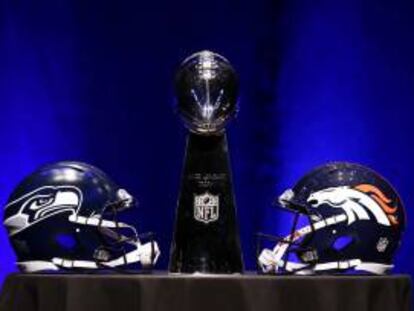 El trofeo Vince Lombardi (c) flanqueado por el casco de los Seattle Seahawks (izq) y el de los Denver Broncos (dcha) antes del inicio de la rueda de prensa de los entrenadores de la Super Bowl XLVIII en Nueva York (Estados Unidos) este viernes 31 de enero de 2014.