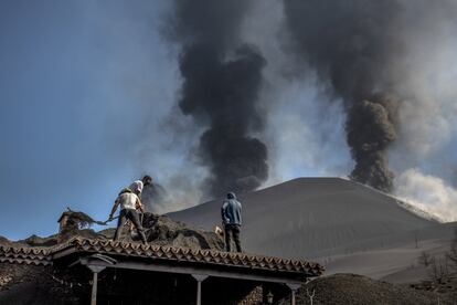 Dos vecinos retiran a pala la ceniza que cubre casi totalmente una casa en Las Manchas. Cientos de personas han tenido que ser desalojadas por el aumento del flujo de lava y ceniza de la erupción del volcán.