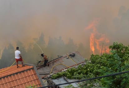 Dois homens jogam água sobre os telhados das casas para protegê-las do fogo.