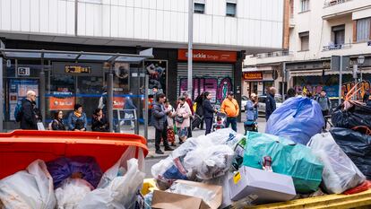 Hilera de pasajeros esperando el autobús en Puente de Vallecas delante de unos cubos de basura sin recoger por la huelga de este martes.