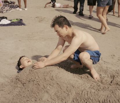 Un padre juega con su hijo enterrándolo en la arena.