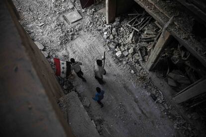 Varios niños sirios caminan con una bandera siria por una calle arrasada, en Duma (Siria).