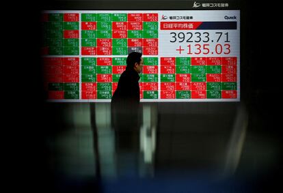 Una persona pasa delante de una pantalla, en Tokio, donde se muestra la evolución del índice Nikkei de Bolsa japonesa.