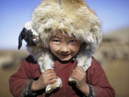 Un niño nómada lleva una oveja sobre los hombros.