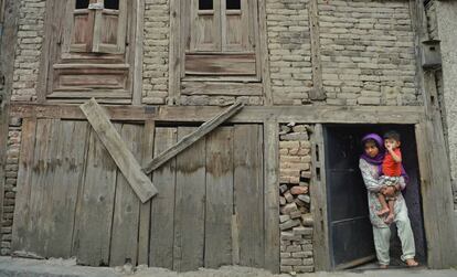 Una niña de la región de Cachemira sujeta en brazos a su hermano en la puerta de su casa mirando una protesta a favor de la independencia de la región y consignas contra India.