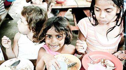 Unos niños huérfanos comen en una sala común.