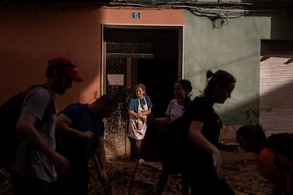 Mar, de 70 a?os, observa como un grupo de voluntarios trabaja para limpiar el lodo que inunda su calle en el centro de Paiporta. Una operacin de rodilla le impide trabajar en la retirada de lodo, por lo que gestiona desde su portal el reparto de agua y alimentos para sus vecinos. Mar ayuda en el trabajo de la floristera de su hermano, en la misma calle, que qued destrozada en la riada. La calle de Mar es uno de los lugares en los que ms muertes se produjeron el martes en esta poblacin del sur de Valencia, viernes 1 de noviembre de 2024.