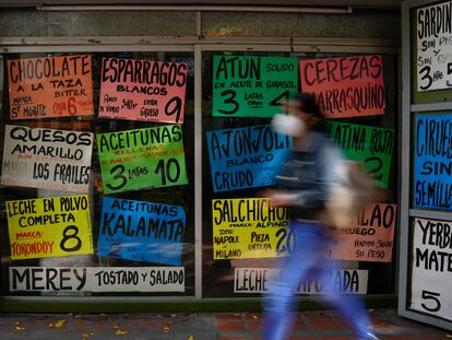 Una mujer camina frente a carteles que muestran los precios de los productos en dólares estadounidenses, afuera de una tienda de comestibles en Caracas (Venezuela).