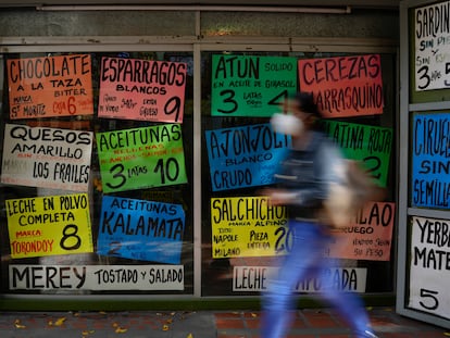 Una mujer camina frente a carteles que muestran los precios de los productos en dólares estadounidenses, afuera de una tienda de comestibles en Caracas (Venezuela).